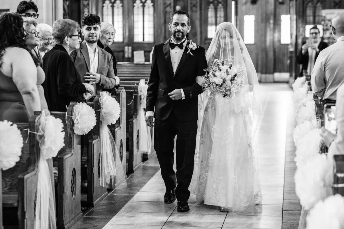 Black and white photo of bride and father walking down the aisle in church