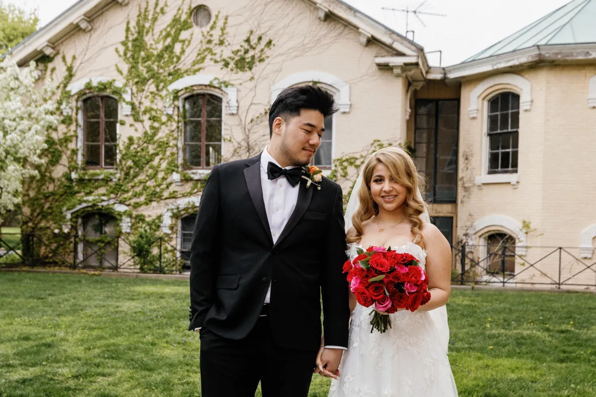 Bride holding flowers and holding grooms hand while groom is looking at her