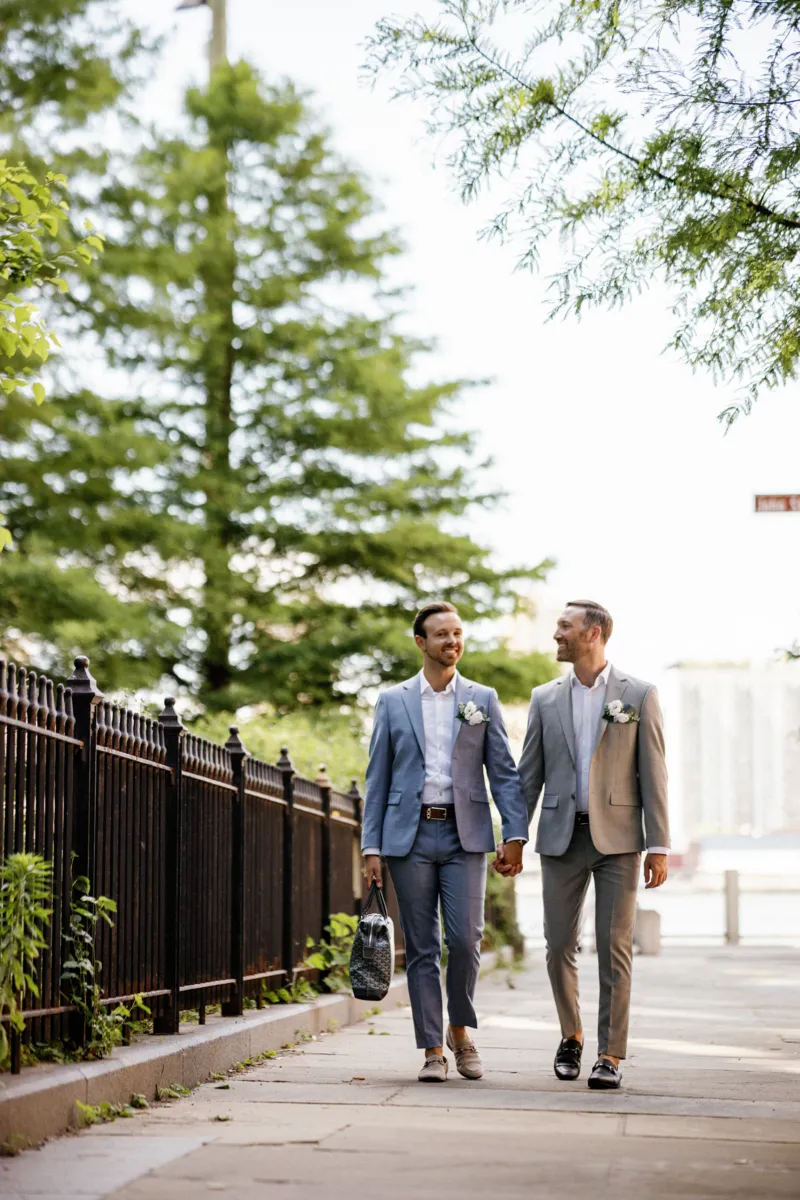 Gay couple holding hands and walking on sidewalk in DUMBO