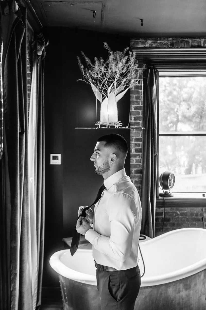 Black and white photo of groom putting his tie on