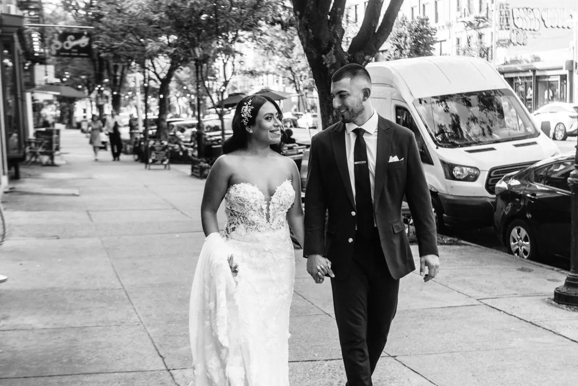 Black and white photo of bride and groom walking on sidewalk