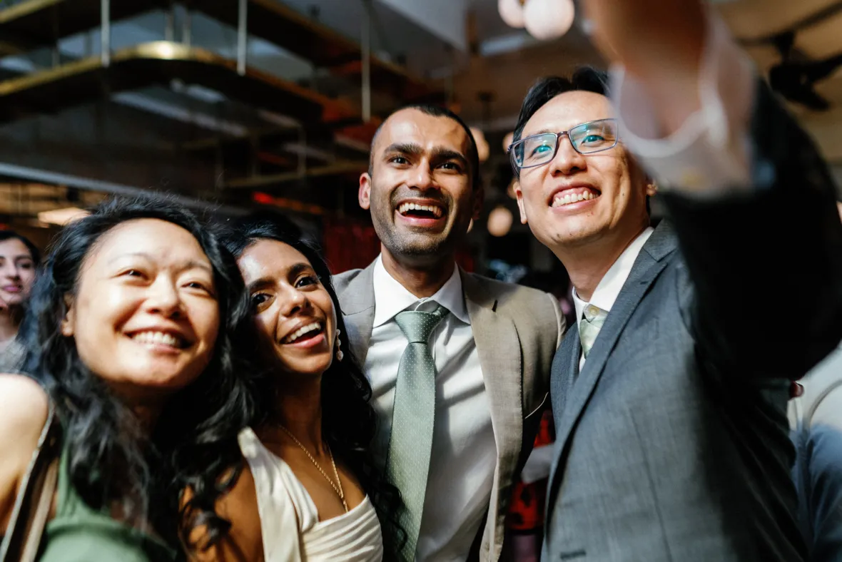 A friend taking a selfie with bride and groom during wedding reception