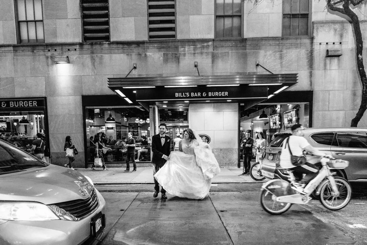 Black and white photo of bride and groom crossing the street